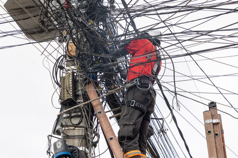 Um homem está numa escada fazendo a manutenção de fios elétricos num poste