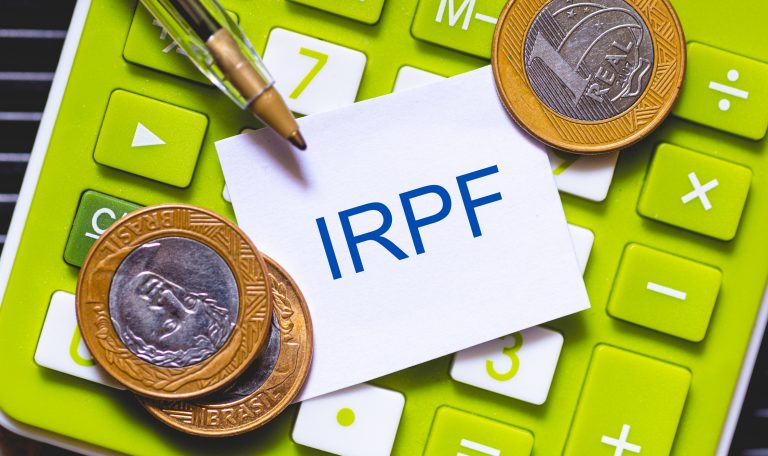 Moedas em cima de uma calculadora e um papel com as letras IRPF
