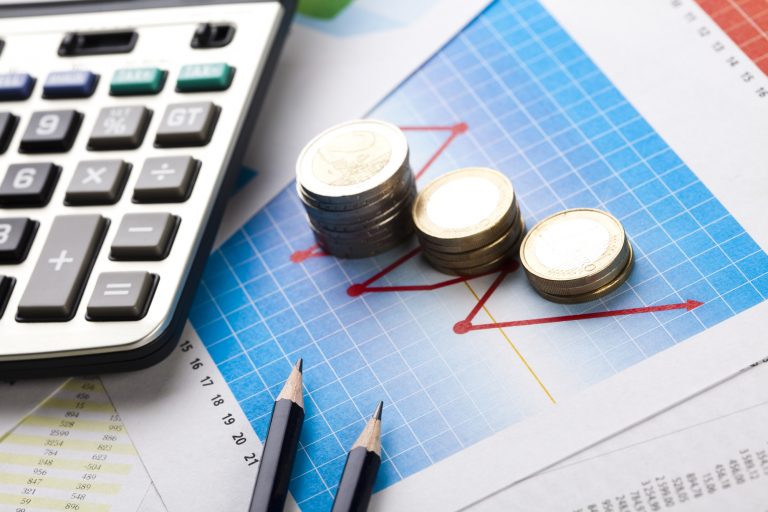 Imagem mostra calculadora, lápis e moedas sobre gráficos impressos