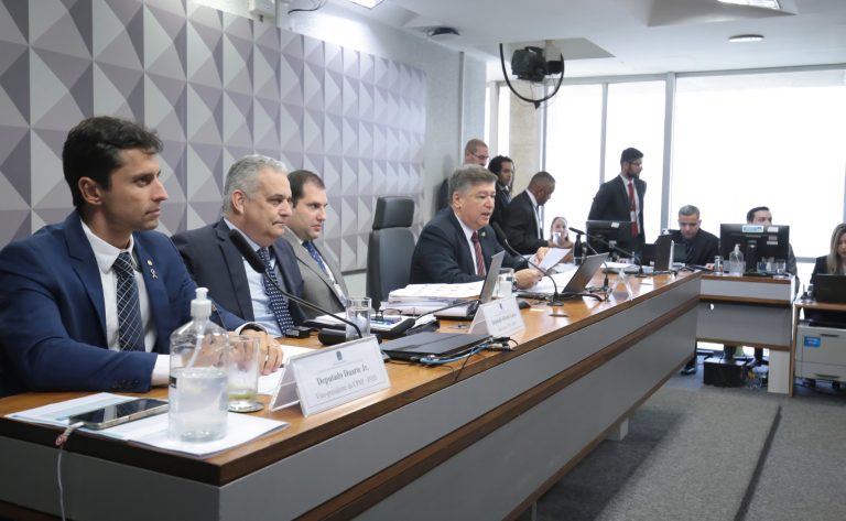 Parlamentares sentados à mesa num plenário