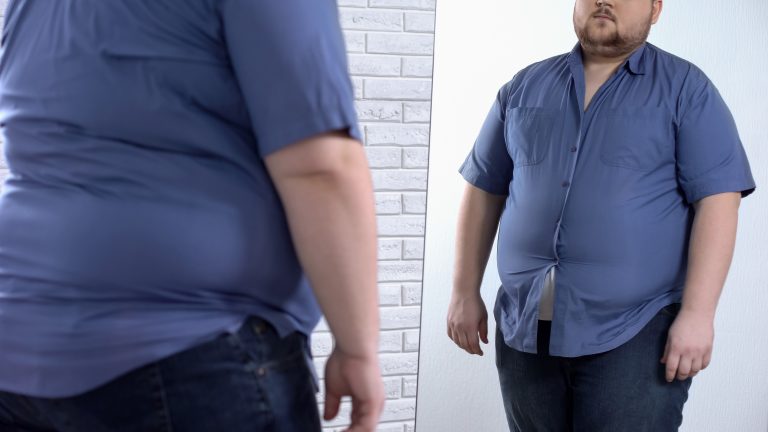 Um homem obeso se olha no espelho