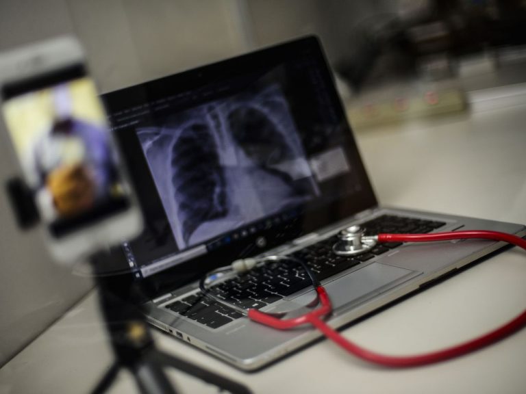 Telemedicina - médico fazendo atendimento pelo celular, computador com imagem de raio X e estetoscópio